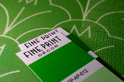 Closeup photo of a green, textured wallpaper sample with color chips laid on top cor color matching