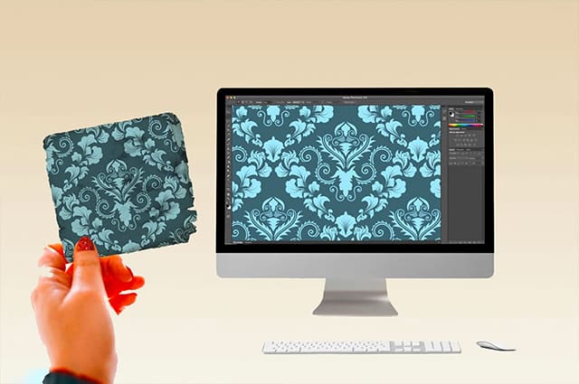 A hand holding a wallpaper sample matches a pattern on a computer screen